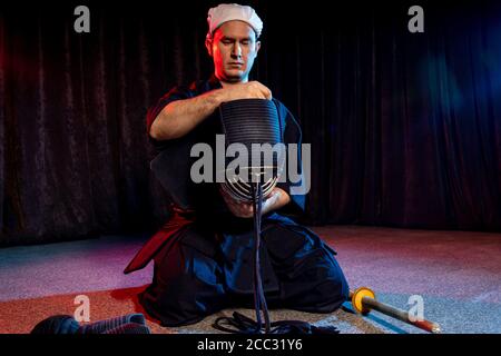 caucasian kendo fighter sit on the floor before fighting, wearing special kendo dress and using all equipment, bamboo sword shinai. japanese martial a Stock Photo