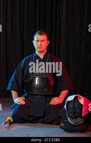 caucasian kendo fighter sit on the floor before fighting, wearing special kendo dress and using all equipment, bamboo sword shinai. japanese martial a Stock Photo