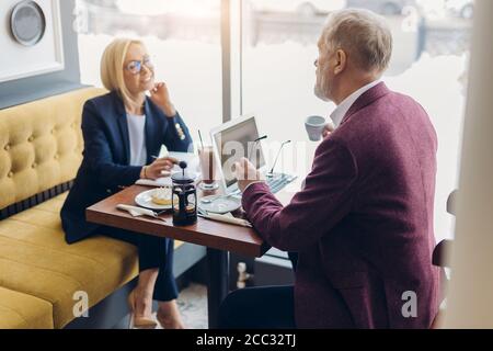 two cheerful senior people having a chat in the modern cafe. close up side view photo, friendly conversation between colleagues Stock Photo