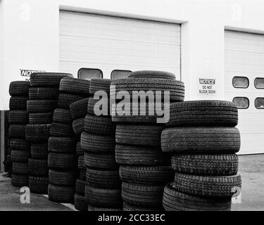 A large wall of mounted automobile tires stands in front of garage doors with a sign reading Do Not Block Doors. The image was captured on analog blac Stock Photo