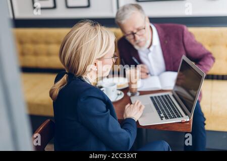 blond girl showing presentation to her partners on notebook. close up photo. two old people working on the project Stock Photo