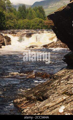 A view of one of the many waterfalls down the River Orchy in Glen Orchy, Scotland showing the rocks, gushing water and surrounding evergreen trees Stock Photo