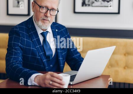 handsome old businessman in glasses with a laptop and coffee posing to the camera,lifestyle. job. profession, freelancer Stock Photo