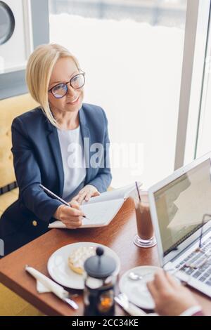 smiling happy young woman in trendy blue suit listening to her partner and writing with a pen. close up photo. freelancer