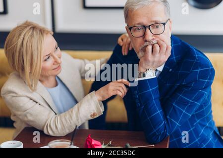 thoughtful offended man doesn't want to talk with a lovely woman while sitting at the cafe.resentful mature elegant man ignoring a beautiful blond wom Stock Photo