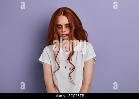 drug addict, drunk girl with long red hair looking at the camera. closeup portrait, isolated blue background, studio shot, girl was arrested by the po Stock Photo