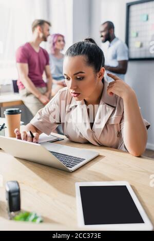 Selective focus of concentrated businesswoman using laptop with multicultural colleagues at background in office Stock Photo