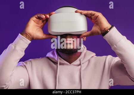 African professional boxer in white hoodie looking through the competition with his participation, using VR glasses, studying mistakes and tactic of o Stock Photo