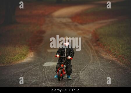 3 year old boy is cycling the red cycle in the park in autumn Stock Photo