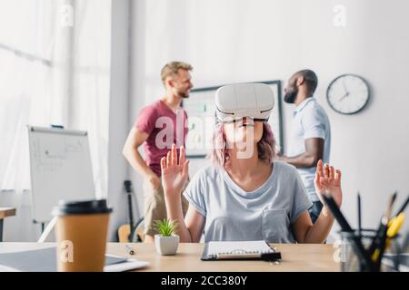 Selective focus of businesswoman using vr headset while multicultural businessmen talking in office Stock Photo