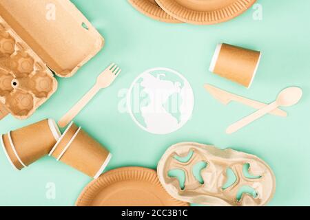 Top view of paper earth sign near disposable tableware and wooden cutlery on green background, ecology concept Stock Photo