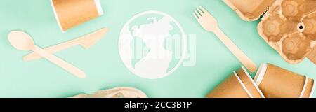 Panoramic shot of disposable tableware and paper earth sign on green background, ecology concept Stock Photo