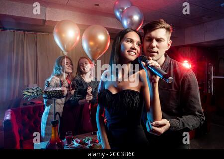 handsome guys and beautiful ladies in dressed have party time in karaoke, modern caucasian people singing in microphone Stock Photo