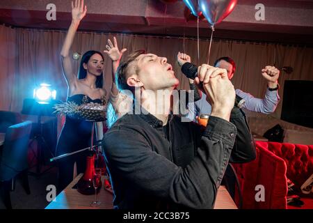 energetic caucasian singer man celebrate birthday in karaoke bar, singing in microphone, rocking and chilling out in singers club. Stock Photo