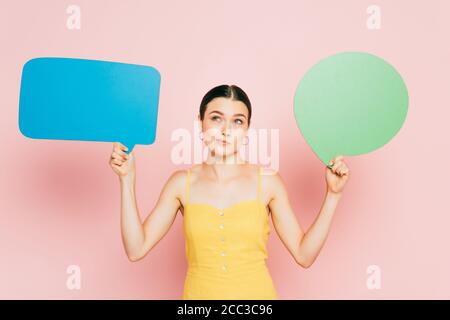pensive brunette young woman with blank speech bubbles on pink Stock Photo