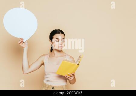 brunette young woman with blank speech bubble reading book on beige Stock Photo