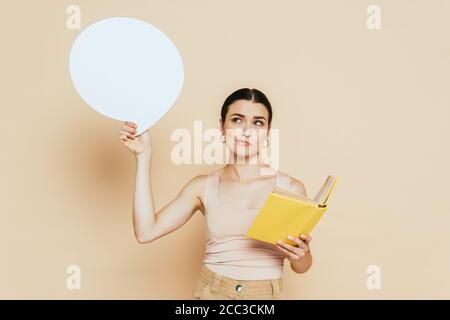 pensive brunette young woman with blank speech bubble reading book on beige Stock Photo