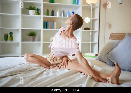 Charming and smilng fitness woman in pajamas doing exercises at home on bed. Healthy lifestyle concept Stock Photo