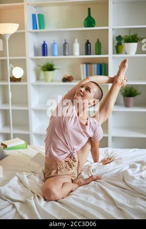 Charming and smilng fitness woman in pajamas doing exercises at home on bed. Healthy lifestyle concept Stock Photo