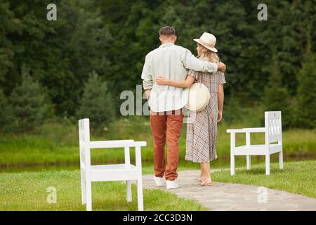 Full length back view portrait of romantic adult couple embracing while walking towards river in rustic countryside scenery, copy space Stock Photo