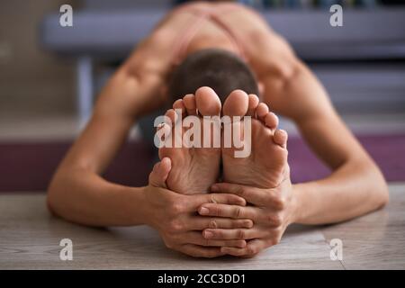 Close up female feet while stretching on mat. Stretching in Seated forward bend exercise, paschimottanasana pose. Woman clothed in sportswear Stock Photo