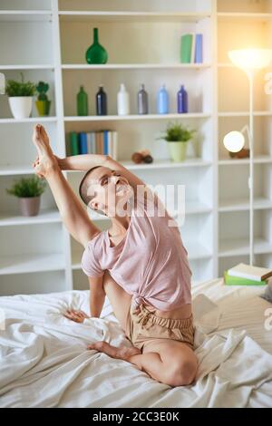 Charming and smilng fitness woman in pajamas doing exercises at home on bed. Healthy lifestyle concept Stock Photo