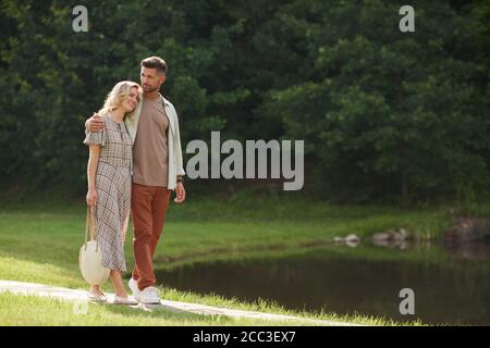 Full length portrait of romantic adult couple embracing while walking towards lake in beautiful nature scenery, copy space Stock Photo