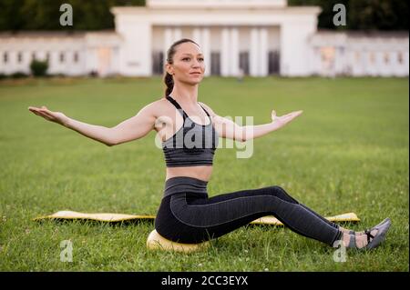 Beautiful young woman lying on a yellow mattress, pose while wearing a tight sports outfit in the park doing pilates or yoga, stretch exercises Stock Photo