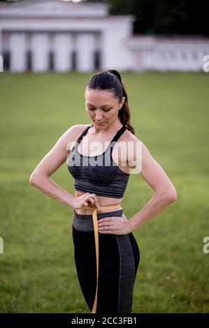 Beautiful young woman, while wearing a tight sports outfit, measures her waist after doing pilates or yoga exercises Stock Photo
