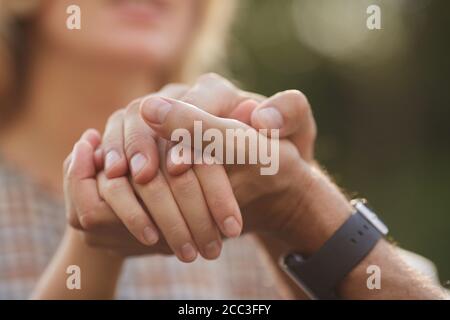 Close up of unrecognizable loving couple holding hands while enjoying romantic date outdoors, focus on foreground, copy space Stock Photo