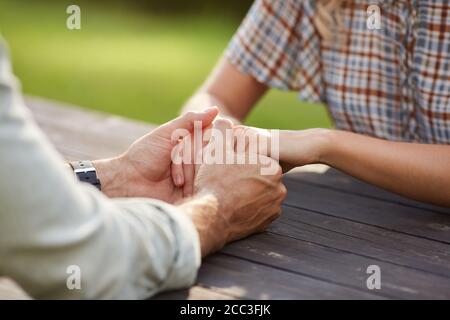 Close up of unrecognizable loving couple holding hands while sitting at wooden table outdoors and enjoying romantic date , copy space Stock Photo