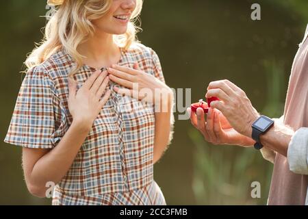 Cropped portrait of unrecognizable man proposing to beautiful girlfriend while standing by lake outdoors in sunlight, copy space Stock Photo