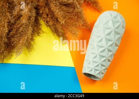 A minimalistic composition of a light turquoise ceramic vase, lies an empty vase on a colored background. Nearby are the branches of dry clumps. Stock Photo