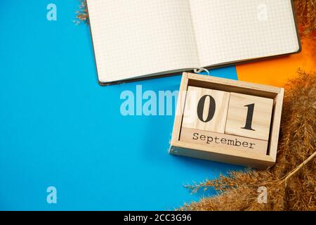 Calendar of wooden cubes with numbers and months. Notepad with white sheets. The first day of the school year. Choosing a number on a wooden calendar. Stock Photo