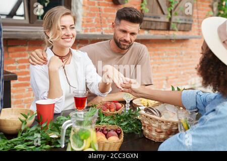 Portrait of beautiful blonde woman showing off engagement ring to friends during outdoor dinner, copy space Stock Photo