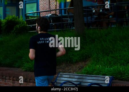 Maryland, USA 08/14/2020: A young white man is running alone  in a street in Frederick. He has wireless earbuds in his ears and he wears a black t shi Stock Photo