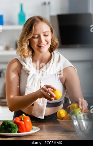selective focus of young woman holding lemons in hands near vegetables Stock Photo