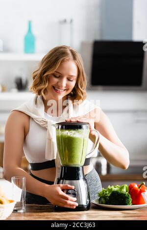 young woman mixing green smoothie in blender near vegetables Stock Photo