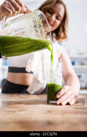 selective focus of woman pouring green smoothie in glass Stock Photo
