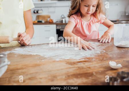 cropped view of mother standing near daughter scattering flour on kitchen table Stock Photo