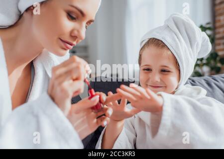 selective focus of young woman in white bathrobe covering fingernails of daughter with red enamel Stock Photo