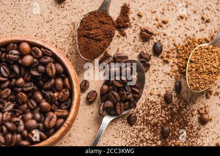 top view of ground, instant coffee and beans in spoons near wooden bowl on beige surface Stock Photo