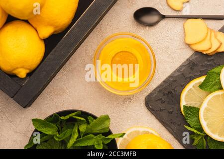 top view of yellow lemons, mint green leaves, ginger root slices and honey on beige concrete surface Stock Photo