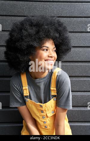 Happy African teen girl with Afro hair laughing standing on black background. Stock Photo