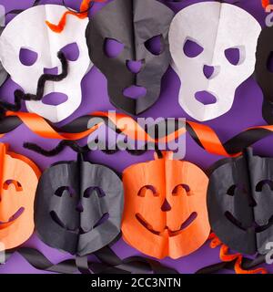 Halloween, holidays and decoration concept - jack-o-lantern pumpkins and skull garland on purple background, traditional autumn october party decor, s Stock Photo