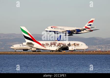 British Airways Airbus A380 arrives at San Francisco as an Emirates Airbus A380 waits for a United Airlines Boeing 777 to depart. Stock Photo