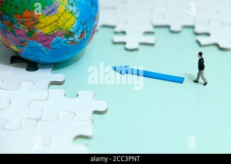 Business strategy conceptual photo - Miniature businessman walking into globe in the middle of jigsaw puzzle