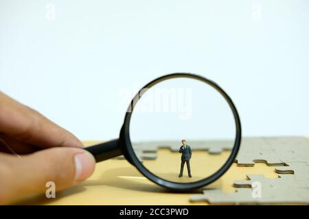 Business strategy conceptual photo - Miniature businessman standing behind magnifier glass in the middle of jigsaw puzzle Stock Photo