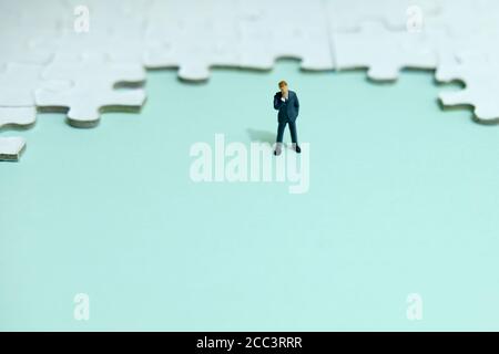 Business strategy conceptual photo - Miniature businessman thinking in front of puzzle jigsaw