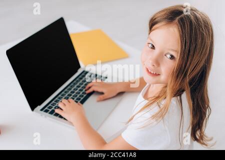 high angle view of girl looking at camera while using laptop with blank screen Stock Photo